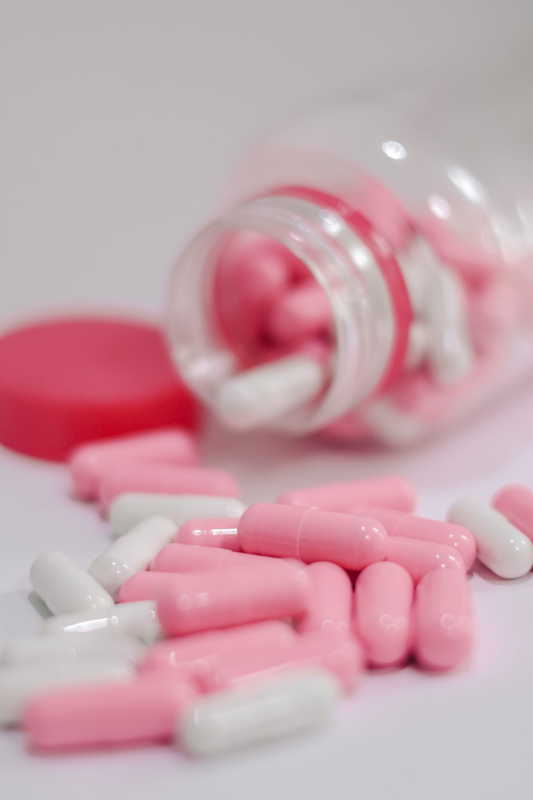 A close-up of pink and white capsules spilled from a bottle, depicting pharmaceuticals and medication.